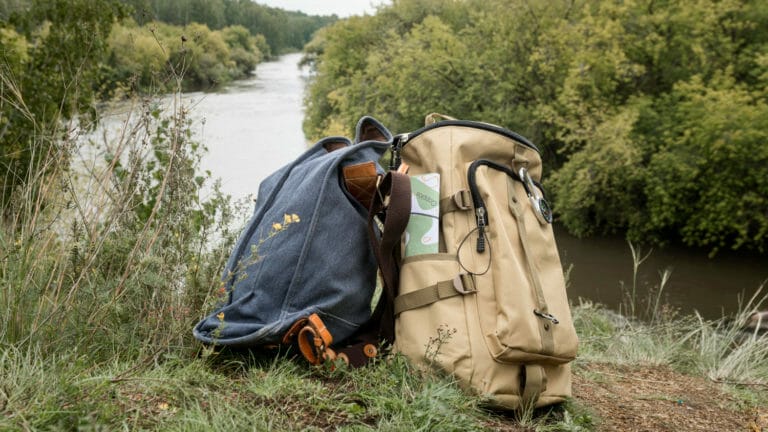 Deux sacs à dos reposent sur l'herbe verdoyante, témoins de l'aventure à venir sur le chemin de Saint-Jacques de Compostelle. Avec en toile de fond une vue sereine sur la rivière, l'image capture l'excitation et la tranquillité qui accompagnent ce pèlerinage spirituel et enrichissant.